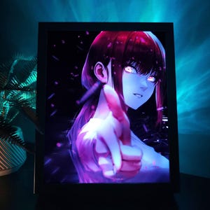 Pode incluir: Uma impressão de arte de anime emoldurada com uma personagem feminina com cabelo ruivo e olhos brilhantes. A obra de arte tem um fundo escuro com detalhes em roxo e rosa. A personagem aponta para o espectador.