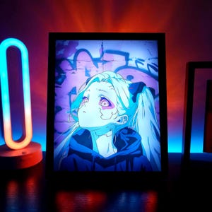Può includere: Stampa artistica anime incorniciata con un personaggio con capelli azzurri e occhi viola, che guarda in alto. L'opera è ambientata contro un muro coperto di graffiti, all'interno di una cornice nera. L'immagine è illuminata da una morbida luce interna.