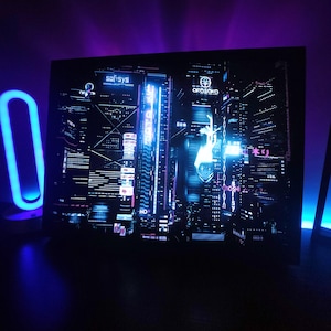 Könnte beinhalten: Ein gerahmter Kunstdruck, der eine futuristische Stadtlandschaft bei Nacht zeigt, beleuchtet von Neonlichtern in Blau, Lila und Rosa. Das Kunstwerk zeigt Wolkenkratzer und japanischen Text. Links ist ein blaues Neonlicht zu sehen.