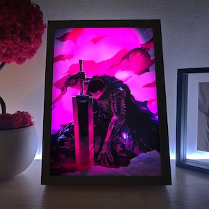 Puede incluir: Una obra de arte enmarcada que presenta una ilustración de estilo manga de un personaje arrodillado con una gran espada. La obra está iluminada con un vibrante resplandor rosa y púrpura, sobre un fondo oscuro. El marco es negro.