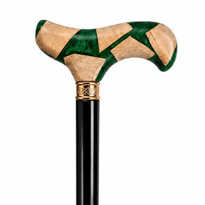 May include: A walking cane featuring a T-shaped handle crafted from segments of light tan burl wood and translucent emerald green resin. A gold-colored metal collar with intricate engraved detailing connects the handle to a smooth black shaft.