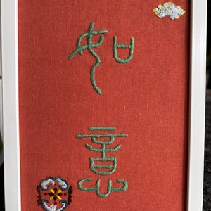Könnte beinhalten: Gerahmte Stickerei mit rotem Hintergrund und weißem Rahmen. Die Stickerei zeigt grüne chinesische Schriftzeichen, eine Wolke und ein Blumenmuster. Ein einzigartiges Stück Wohnkultur.
