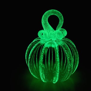 Puede incluir: Una calabaza de vidrio verde con un tallo en espiral y una superficie texturizada. La calabaza brilla en la oscuridad.