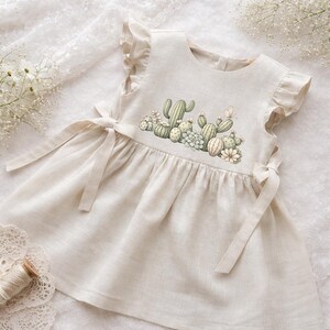 Puede incluir: Vestido de lino beige claro con diseño de cactus y suculentas. El vestido presenta mangas con volantes y lazos en los laterales. El vestido está diseñado para un niño.
