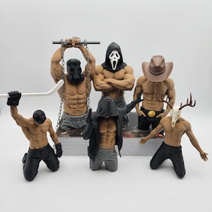 May include: A collection of six muscular male torso figurines. One wears a gas mask with chains, one a ghost mask, one a cowboy hat, one a hooded cloak, one a deer skull mask, and one holds a white hockey stick. All figures are shirtless.