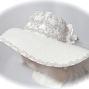 Puede incluir: Un sombrero blanco de ala ancha para el sol con un borde de encaje y un adorno de flor blanca.