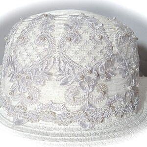 Puede incluir: Sombrero de sol blanco con ala ancha y adorno de encaje blanco con detalles de perlas.