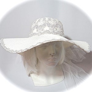 Puede incluir: Un sombrero blanco de ala ancha para el sol con un borde de cuentas y un dise&ntilde;o de encaje en la corona.