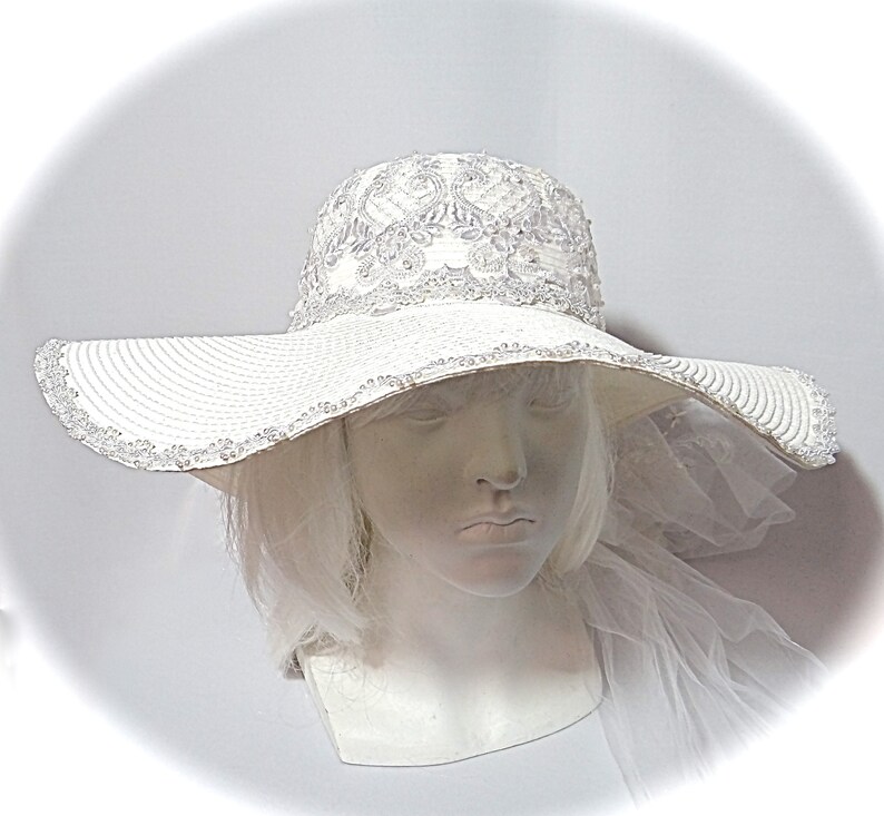 Puede incluir: Un sombrero blanco de ala ancha para el sol con un borde de cuentas y un dise&ntilde;o de encaje en la corona.