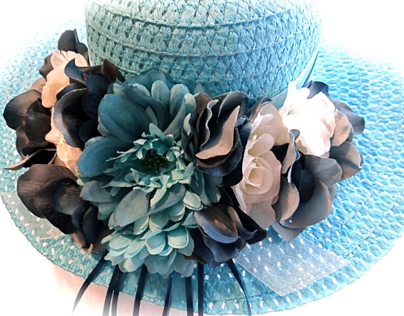 May include: A light blue straw hat with a wide brim and a large flower embellishment. The flower is made of white, blue, and dark blue fabric.