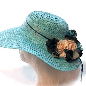 May include: A light blue straw hat with a wide brim and a black ribbon. The hat is decorated with a cluster of white and black fabric flowers.
