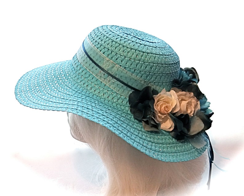 May include: A light blue straw hat with a wide brim and a black ribbon. The hat is decorated with a cluster of white and black fabric flowers.