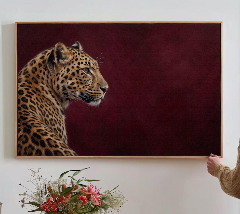 May include: A rectangular wall art print featuring a profile view of a leopard with golden fur and black spots. The leopard is positioned on the left side against a solid, deep burgundy background. The artwork is encased in a thin wooden frame.