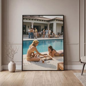 Puede incluir: Impresión enmarcada de una escena de fiesta en la piscina vintage. Dos personas en traje de baño juegan al backgammon junto a la piscina. Un grupo de personas socializan cerca de la piscina y una casa grande. La imagen tiene una estética retro.