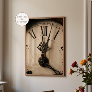 Peut inclure: Impression d'horloge vintage encadrée avec des chiffres romains et des aiguilles décoratives. Le cadran est blanc cassé avec des chiffres noirs et un mécanisme d'horloge en métal foncé. L'impression est dans un cadre en bois brun clair.
