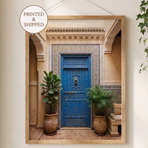 May include: Framed print featuring a vibrant blue door with detailed carvings, set within an arched entryway. The image includes potted plants and decorative tilework. The print is labelled "PRINTED & SHIPPED".