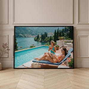 Peut inclure: Une affiche encadrée représentant un paysage de lac et de montagnes, avec deux personnes se relaxant au bord d'une piscine. L'une lit un magazine, l'autre tient une boisson. La scène se déroule en extérieur ensoleillé.