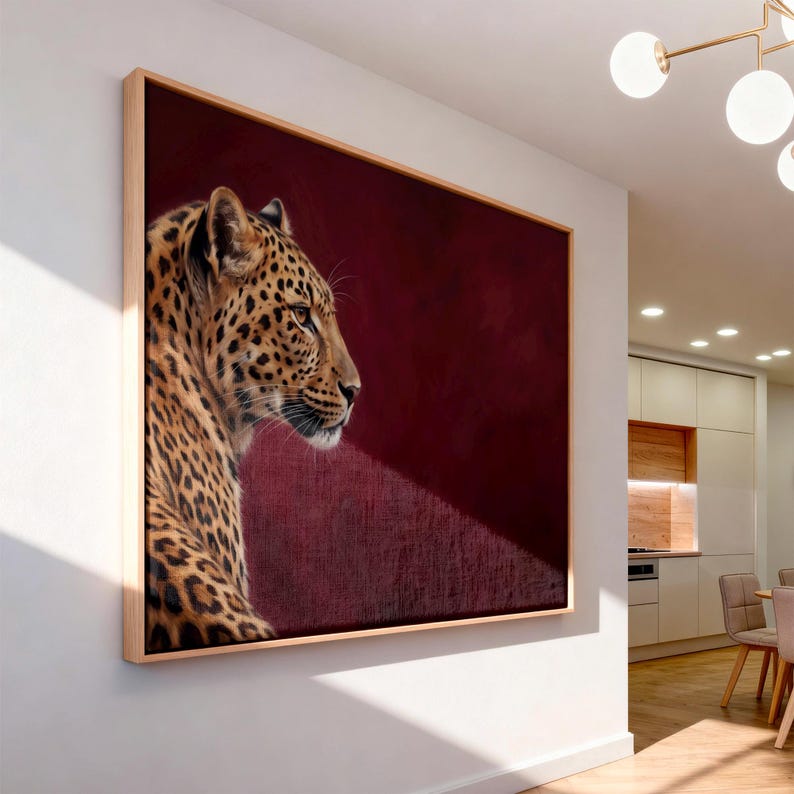 May include: A rectangular wall art piece featuring a profile portrait of a leopard with golden fur and black spots. The leopard is positioned on the left side against a deep, solid burgundy background. The artwork is encased in a light wood frame.