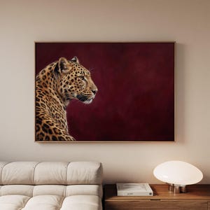May include: A rectangular wall art print featuring a profile view of a leopard with golden fur and black rosettes. The leopard is positioned on the left side of the frame against a solid, deep burgundy red background, enclosed in a thin frame.