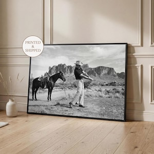 May include: Monochrome framed print depicting a golfer swinging a club on a desert golf course, with a saddled horse. The print is in a black frame and has the text "PRINTED & SHIPPED" in a circle.