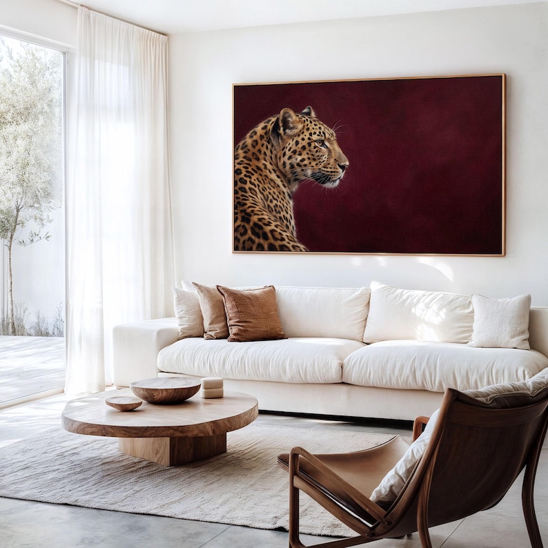 May include: A rectangular wall art print featuring a profile view of a leopard with a spotted coat against a solid deep burgundy background. The artwork is encased in a thin, light-toned wooden frame and is displayed horizontally on a wall.