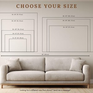 May include: A beige sofa with two cushions positioned below a wall chart titled CHOOSE YOUR SIZE. The chart displays various rectangular dimensions in inches and centimeters, ranging from 16x12 inches to 48x32 inches, with a sofa width of 85 inches.