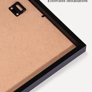 May include: Close-up of a black picture frame with a brown backing. The frame has a hanging bracket attached. Text on the image reads "Ready to hang" and "Effortless installation".