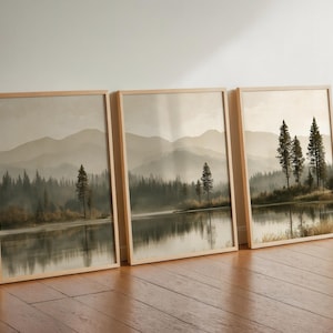 Peut inclure: Un ensemble de trois cadres muraux représentant un paysage composé d'un lac calme, d'une forêt dense de pins et de montagnes lointaines dans une palette de couleurs sépia atténuées. Chaque impression est encadrée de bois clair.