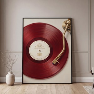 Può includere: Una stampa artistica incorniciata raffigurante un disco in vinile rosso intenso su un giradischi con un braccio dorato. L'etichetta centrale è color crema con il testo The Ruby Edition Collector's Series e un piccolo emblema dorato stampato.