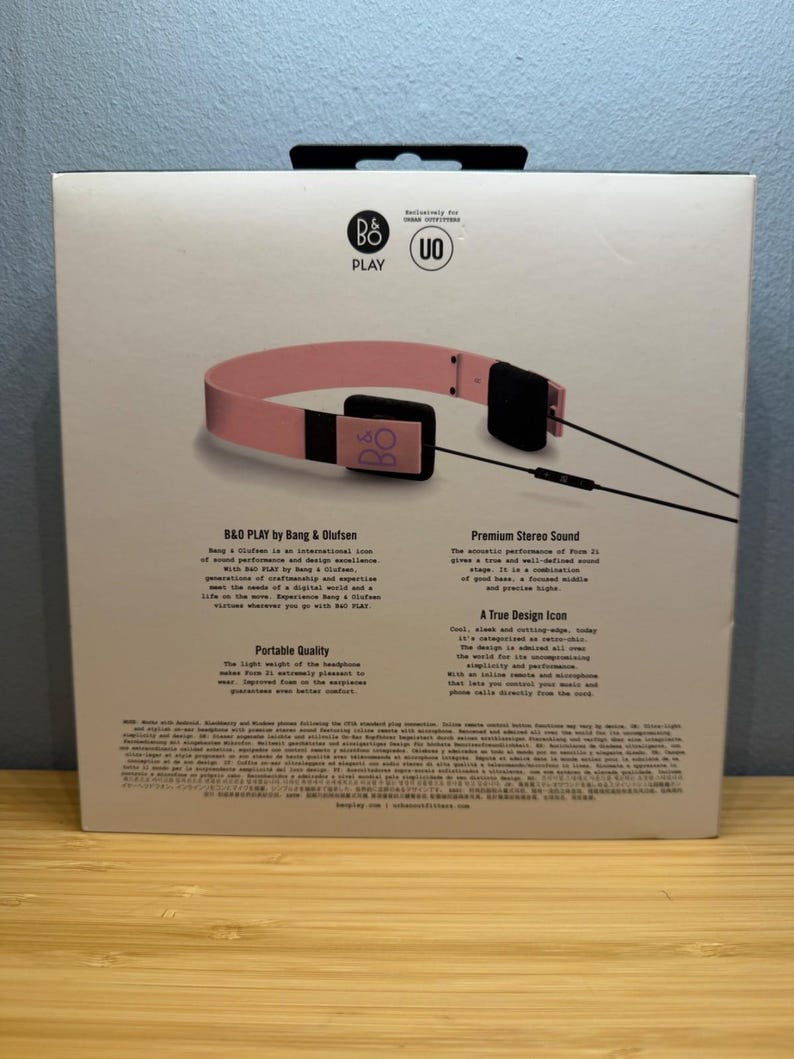 May include: A box featuring pink B&O PLAY headphones. The headphones have a pink headband and black earcups. The box has text that reads "B&O PLAY by Bang & Olufsen" and "Premium Stereo Sound".