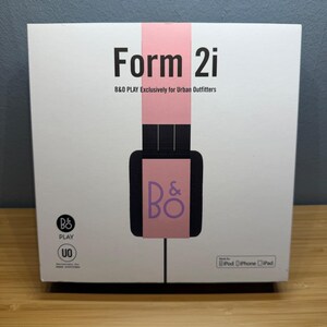May include: White box with the text "Form 2i" in black, and "B&O PLAY Exclusively for Urban Outfitters" below it. A pink vertical stripe runs down the center, with a black headphone graphic and the "B&O" logo. The box is for iPod, iPhone, and iPad.