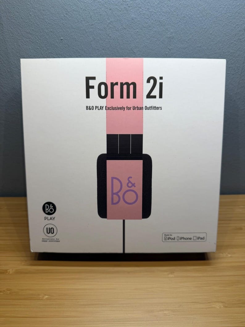 May include: White box with the text "Form 2i" in black, and "B&O PLAY Exclusively for Urban Outfitters" below it. A pink vertical stripe runs down the center, with a black headphone graphic and the "B&O" logo. The box is for iPod, iPhone, and iPad.