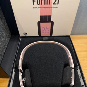 May include: Pink Form 2i headphones in a black box with the text "Form 2i" and "B&O PLAY Exclusively for Urban Outfitters" on the box. The headphones are displayed on a black foam insert.