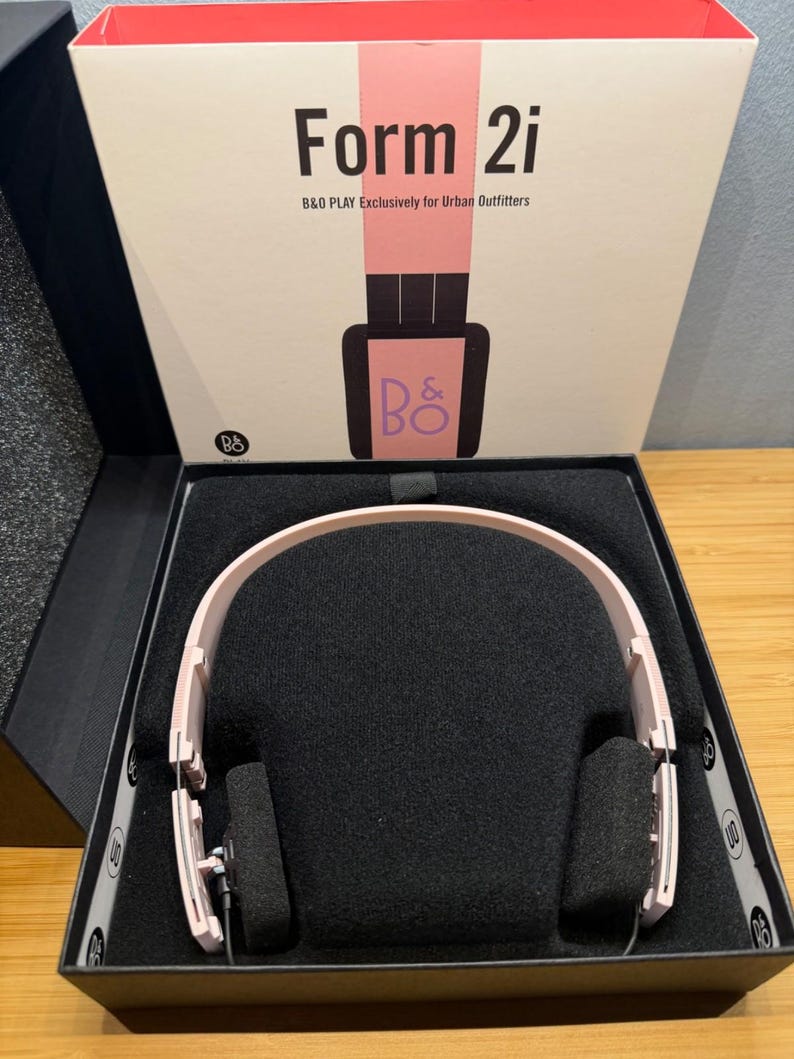 May include: Pink Form 2i headphones in a black box with the text "Form 2i" and "B&O PLAY Exclusively for Urban Outfitters" on the box. The headphones are displayed on a black foam insert.