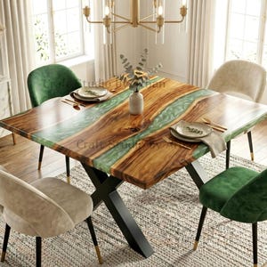 May include: A square dining table featuring a natural wood grain surface with a central translucent green resin inlay, supported by a black metal X-shaped base. The table is surrounded by four upholstered chairs in alternating green and beige colours.