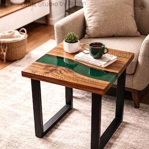 Puede incluir: Pequeña mesa auxiliar cuadrada con tapa de madera y patas de metal negro. La encimera presenta un río de resina epoxi verde. Una pequeña planta, una taza y un libro descansan sobre la mesa. El texto "Craft Studio by Arhan" es visible.