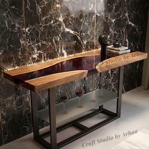 May include: A modern console table with a live edge wooden top and a deep red resin inlay. The table has a black metal frame and a glass shelf. The top is approximately 152 cm long.