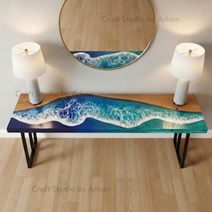 May include: A wooden and resin bench featuring a wave design in blue and white hues. The bench has black metal legs and is accompanied by two white table lamps. A round mirror with a similar wave design is above. The text "Craft Studio by Arhan" is visible.