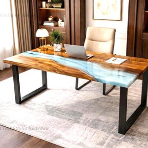 May include: A wooden desk with a blue resin river design. The desk has a rectangular top with a natural wood grain finish and black metal legs. A laptop, notepad, and small plant are on the desk. The desk is in a home office setting.
