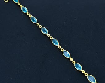 May include: A gold bracelet with oval, light blue gemstones. The gemstones are linked by small gold chain links. The bracelet has a clasp. The bracelet's length is approximately 18 cm.