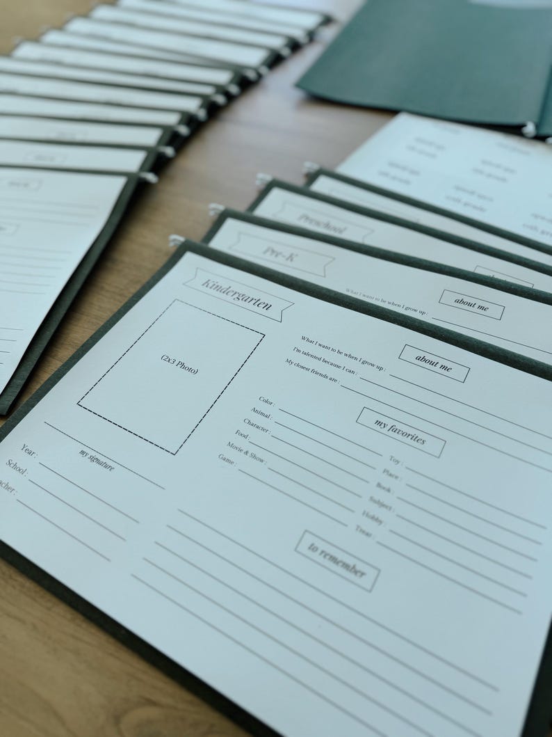 May include: A set of white paper folders with black text. The folders are labeled with the words "Kindergarten", "Pre-K", and "about me". The folders are designed for children to record their favorite things, interests, and memories.