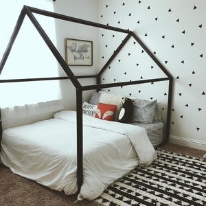 May include: A black wooden canopy bed frame with a white bedspread and pillows. The bed is decorated with a red and white pillow with the words "Never Give Up" and a black and white penguin pillow. The wall behind the bed is decorated with black triangle stickers.