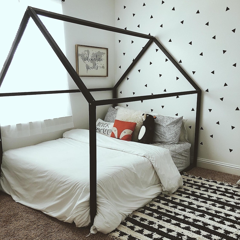 May include: A black wooden canopy bed frame with a white bedspread and pillows. The bed is decorated with a red and white pillow with the words "Never Give Up" and a black and white penguin pillow. The wall behind the bed is decorated with black triangle stickers.