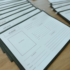 May include: A stack of white paper forms with a green border. The forms are labeled "1st grade", "2nd grade", and "3rd grade". Each form has a space for a photo, a section for personal information, and a section for a signature.