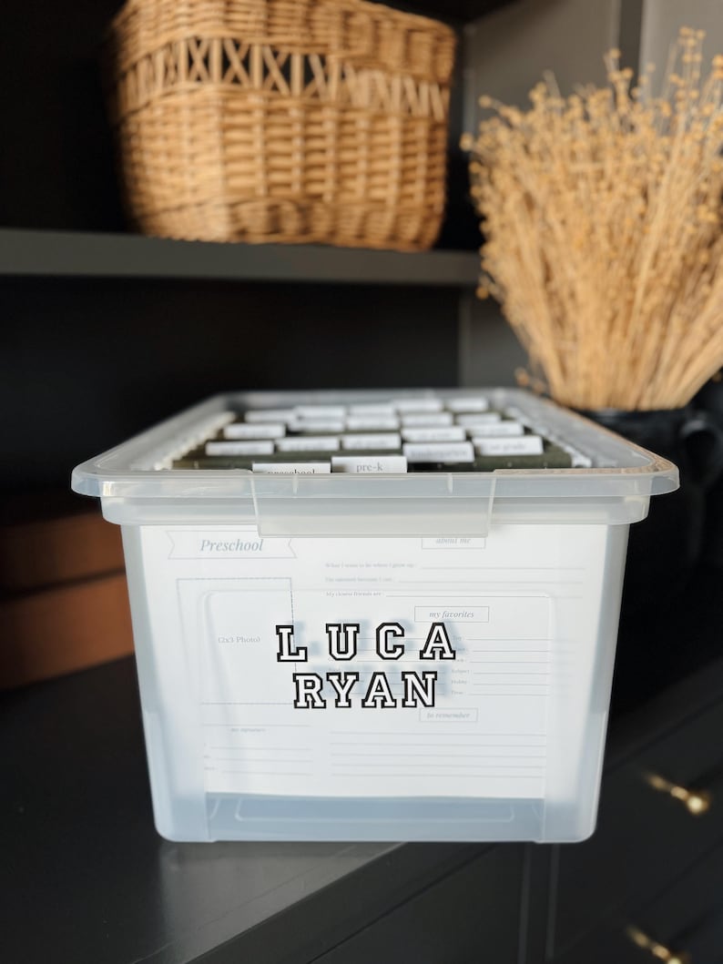 May include: A clear plastic storage bin with a white label that says "Preschool" and has the name "Luca Ryan" written in black letters. The bin is filled with labeled file folders.