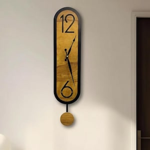 May include: A vertical wooden wall clock with a black frame and a pendulum. The clock face is a light brown color with black numbers at the top and bottom. The clock hands are black. The pendulum is a small, round wooden disc.