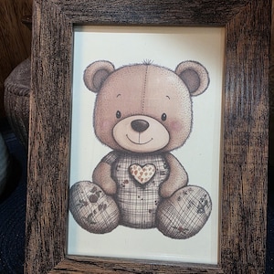 Peut inclure: Impression encadrée d'un ours en peluche de dessin animé avec un cœur sur la poitrine. L'ours brun a des accents à carreaux, dans un cadre en bois brun foncé et rustique.