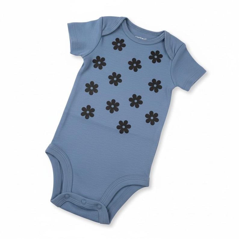 Puede incluir: Un body de beb&eacute; azul claro con mangas cortas y cierre de botones a presi&oacute;n. El body est&aacute; decorado con un estampado de flores de margarita negras. La prenda es de material suave.