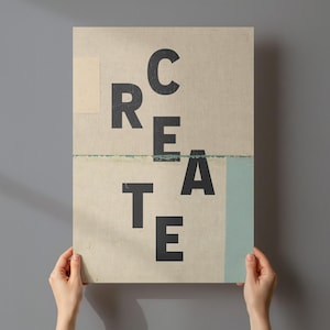 Op de afbeelding: Een rechthoekige poster met het woord "CREATE" in grote, zwarte, schreefloze letters. De poster heeft een beige achtergrond met een lichtblauwe streep en een klein beige vierkant. De poster wordt door twee handen vastgehouden.
