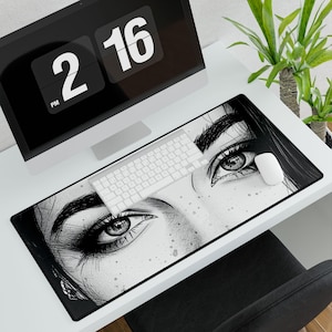 Puede incluir: Una configuración de escritorio en blanco y negro con un monitor de computadora que muestra la hora, un teclado blanco y un ratón. La alfombrilla de escritorio presenta una ilustración detallada de los ojos de una mujer. Una pequeña planta verde está en el fondo.